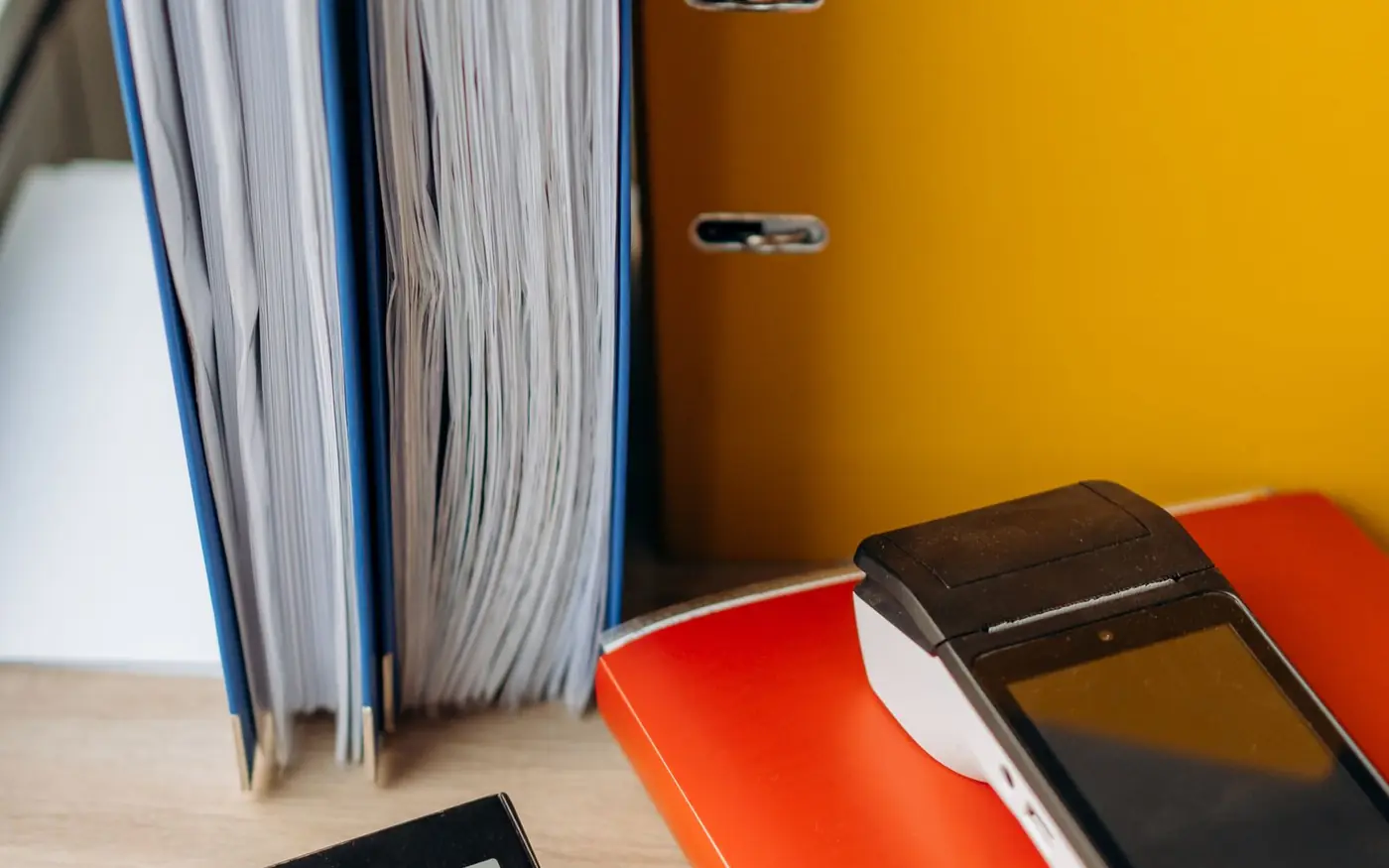 Archivadores llenos de documentación y un datáfono sobre la mesa de un negocio